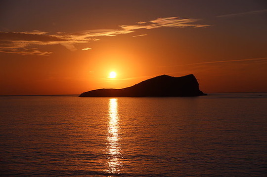 Sun setting behind an island silhouette over a calm sea