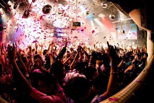 Packed nightclub crowd with hands raised under confetti and mirror balls